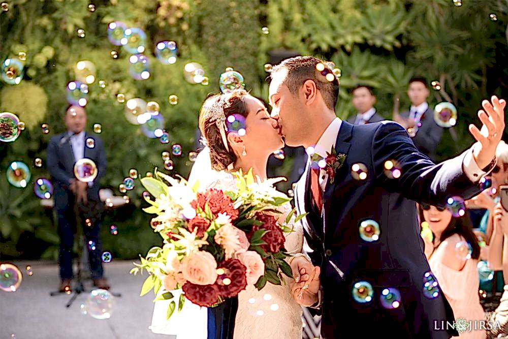 Lin and Jirsa photographing a Chinese wedding in front of the Grand Exit Smog Shoppe in Los Angeles with Orange Blossom Events at 2651 S La Cienega Blvd, Los Angeles, CA 90034 A Chinese couple kissing and getting married with bubbles gently floating above, set against a green forest background