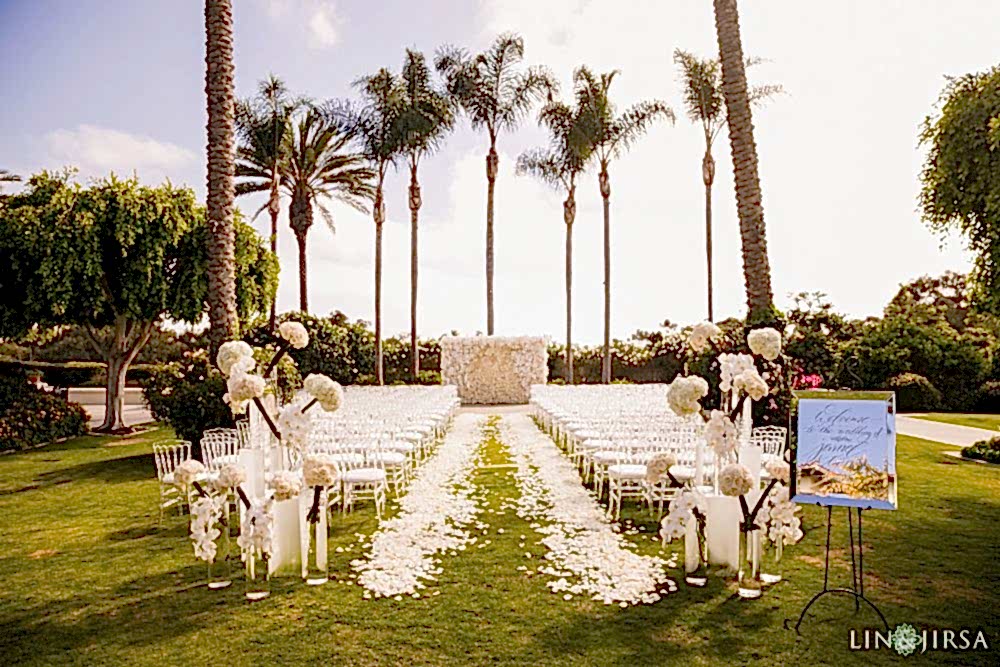 A wedding ceremony photograph shot by Lin and Jirsa Los Angeles at the Park Hyatt Aviara San Diego white wedding altar on a big green lawn with palm trees and blue skies Park Hyatt Aviara San Diego white wedding altar on the lawn with palm trees