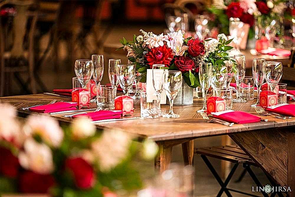 Elegant Chinese wedding reception decor shot by Lin and Jirsa Los Angeles Wedding Photography with Orange Blossom Special Events Beautiful red and pink carnation and rose flower bouquets on a rustic wooden table with silverware and bright pink cloth napkins